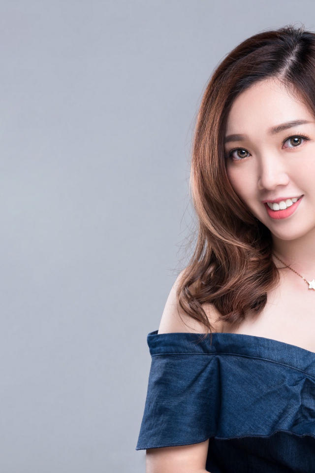 Улыбающаяся девушка азиатка с часами на руке на сером фоне