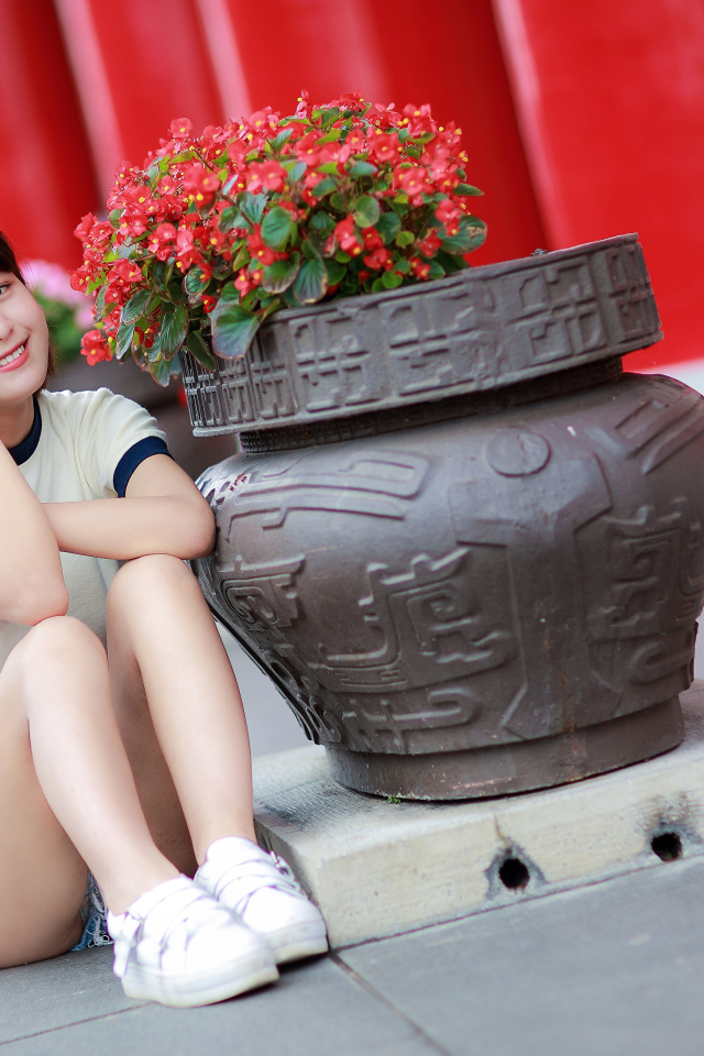 Улыбающаяся азиатка сидит у клумбы с цветами