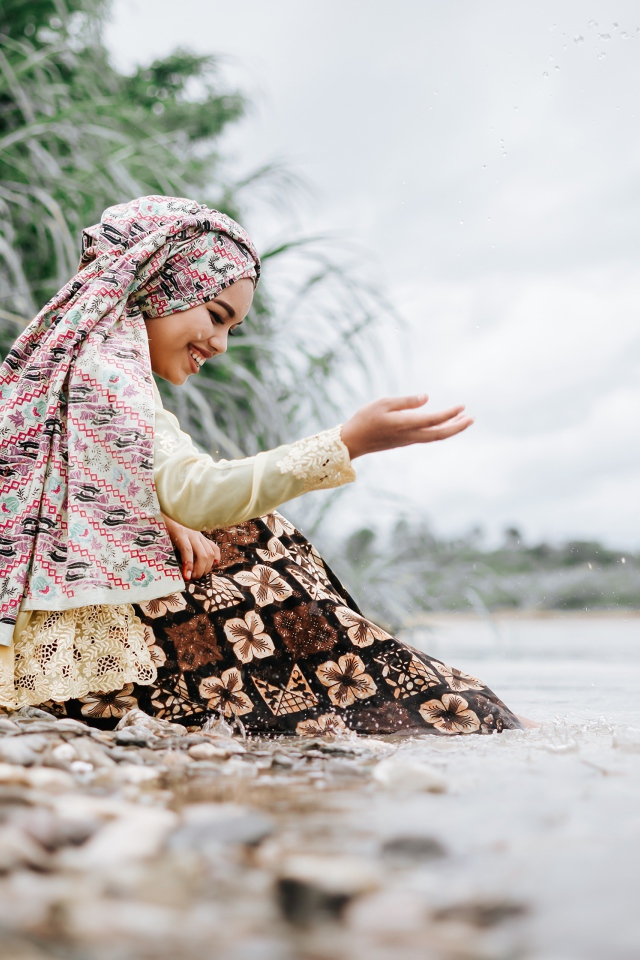 Улыбающаяся девушка азиатка сидит у воды