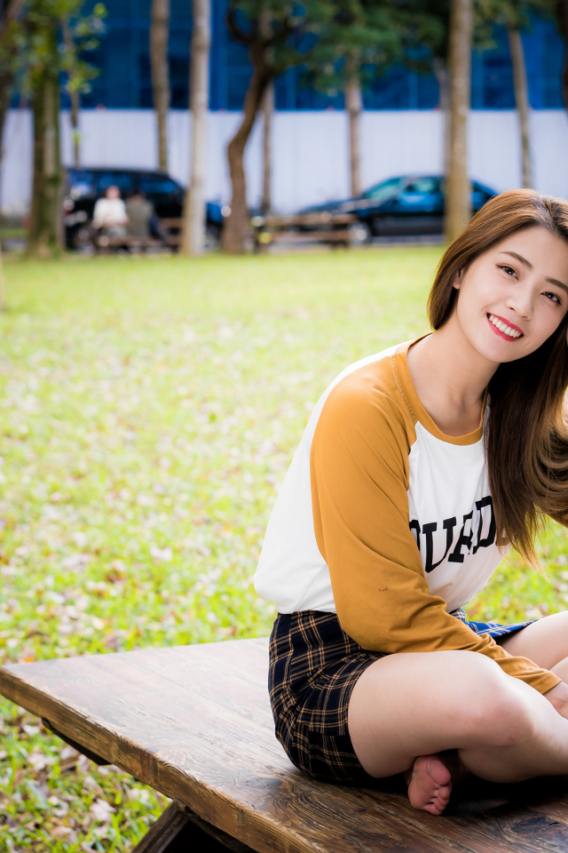 Улыбающаяся девушка азиатка сидит на лавке в парке 