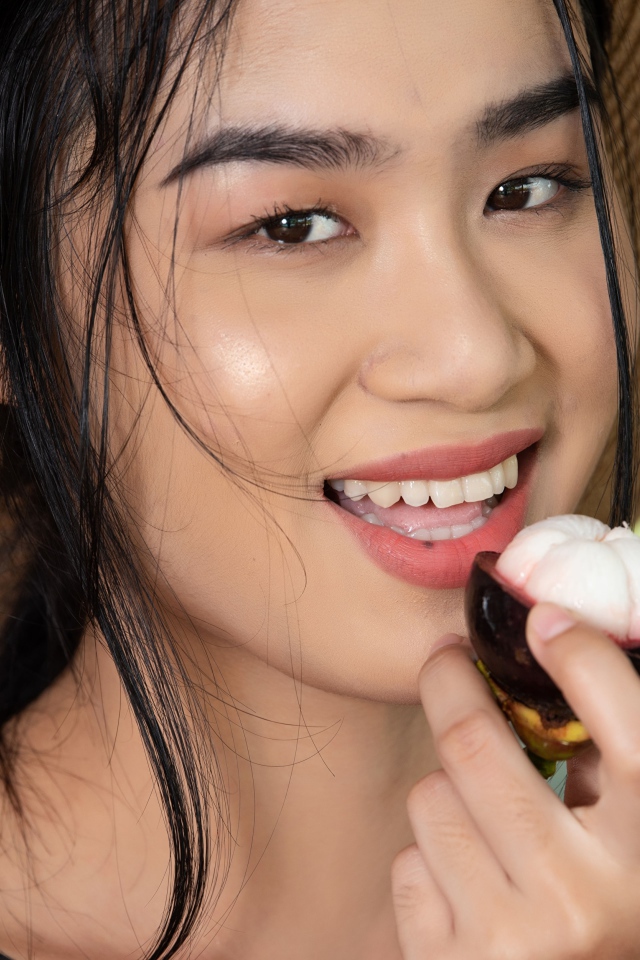 Улыбающаяся азиатка в шляпе с фруктом в руке