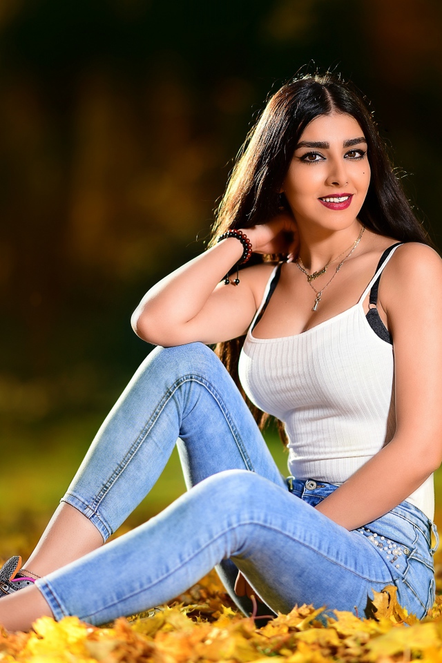 Улыбающаяся брюнетка сидит на опавшей листве