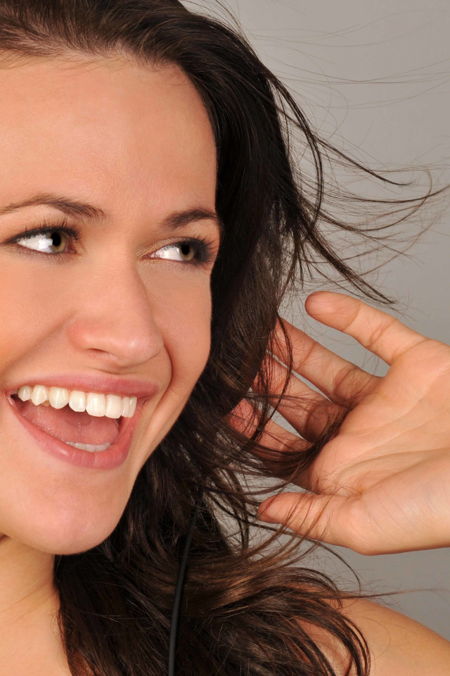 Улыбающаяся девушка в наушниках на сером фоне 