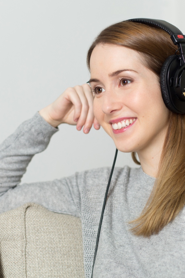 Улыбающаяся девушка в наушниках на диване