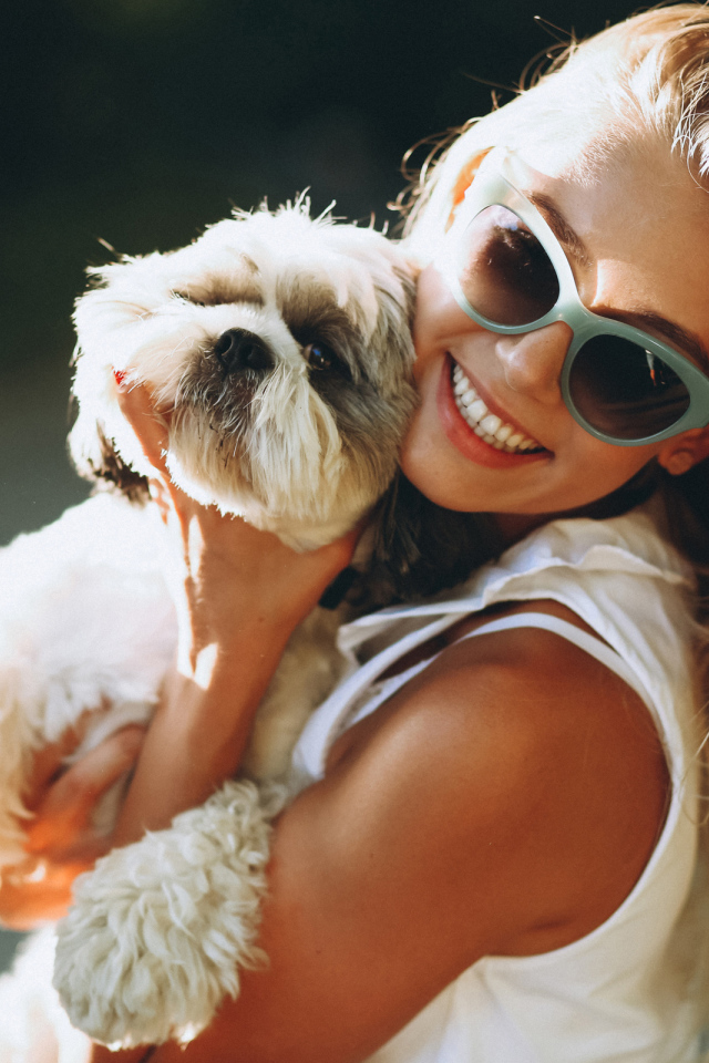Улыбающаяся девушка в солнечных очках с собакой на руках