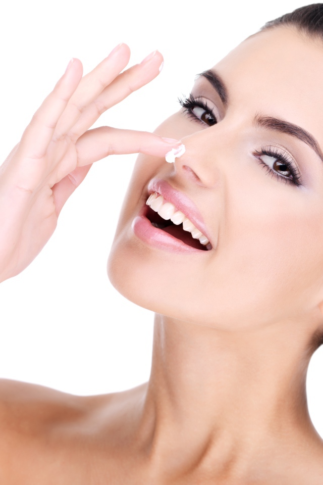 Улыбающаяся девушка мажет крем на нос 