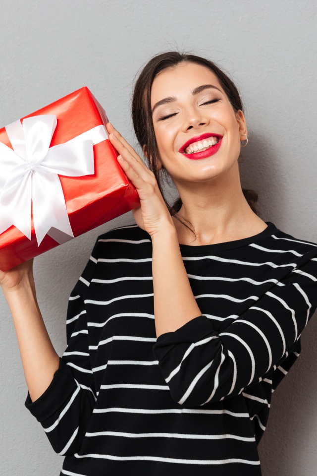 Улыбающаяся девушка с подарком в руках на сером фоне 