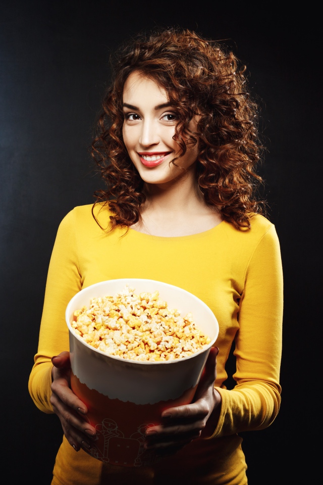 Улыбающаяся девушка с попкорном в руках на черном фоне 