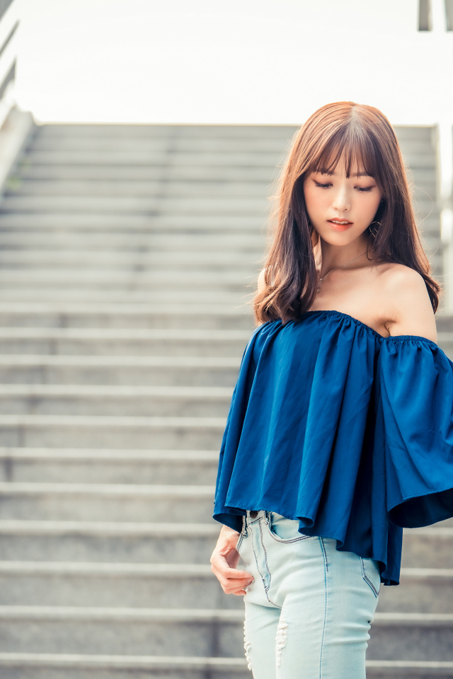 Стильная девушка азиатка с опущенной головой стоит на ступеньках 