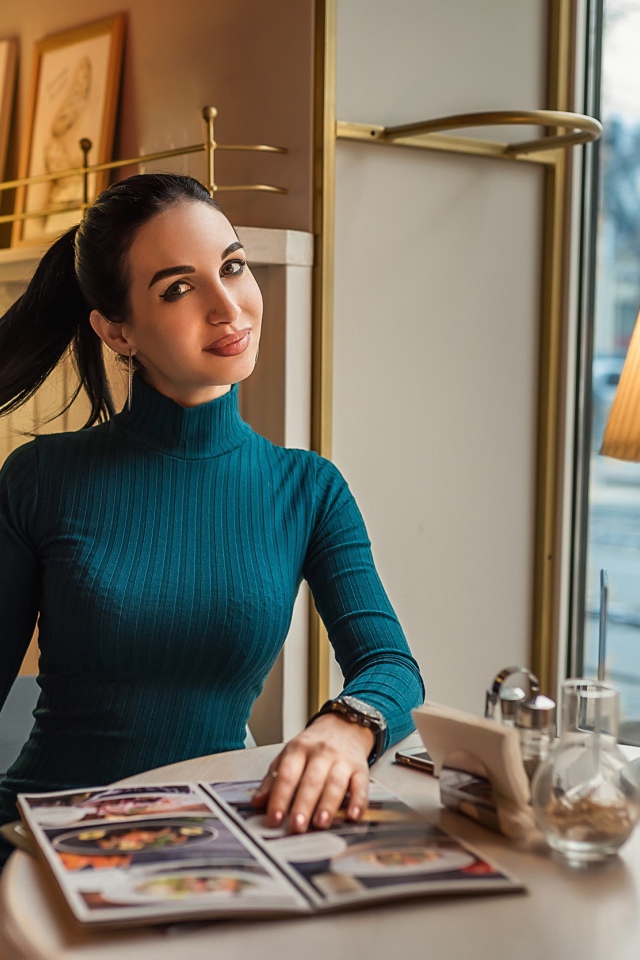 Стильная девушка в платье сидит в кафе у окна