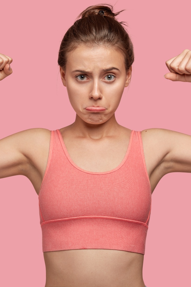 Расстроенная девушка без накаченных рук на розовом фоне