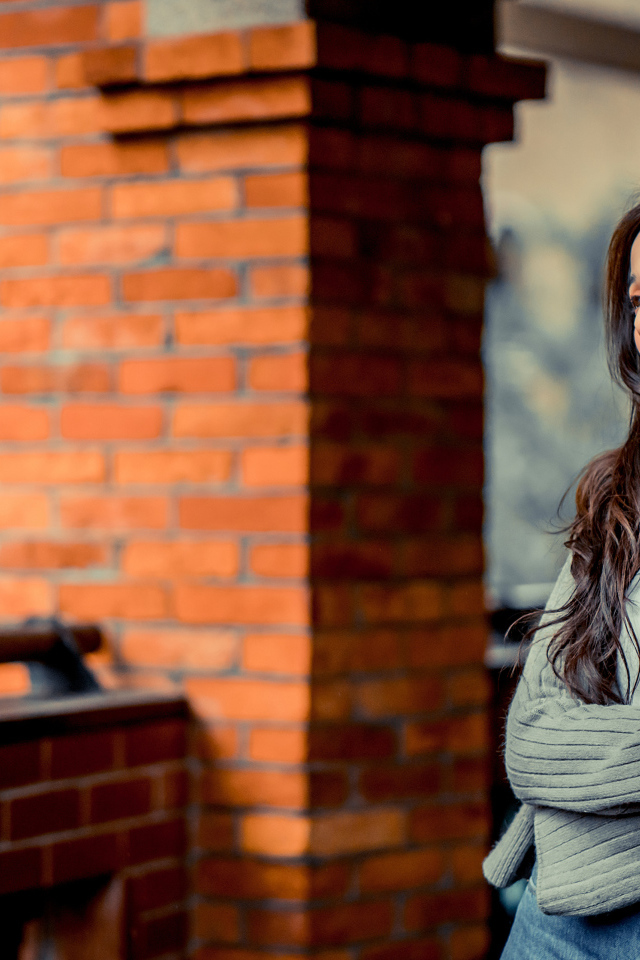 Молодая девушка азиатка в серой кофте у кирпичной стены 