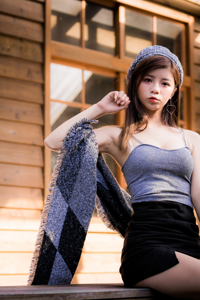 Молодая девушка азиатка в короткой юбке сидит на подоконнике 