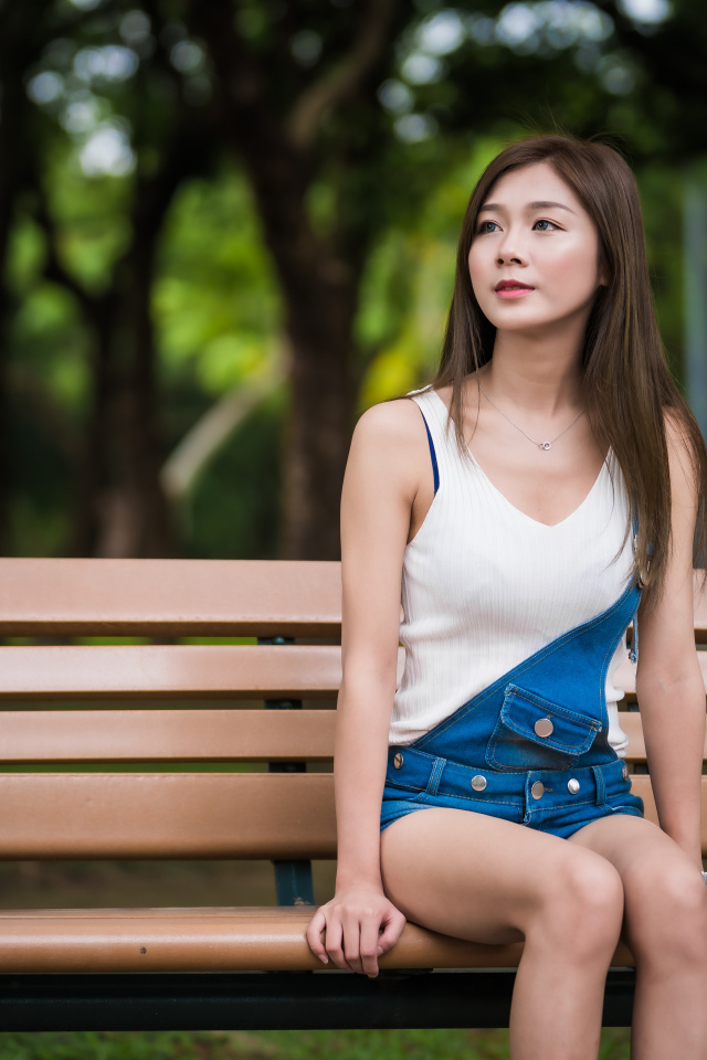 Молодая девушка азиатка сидит в парке на лавочке