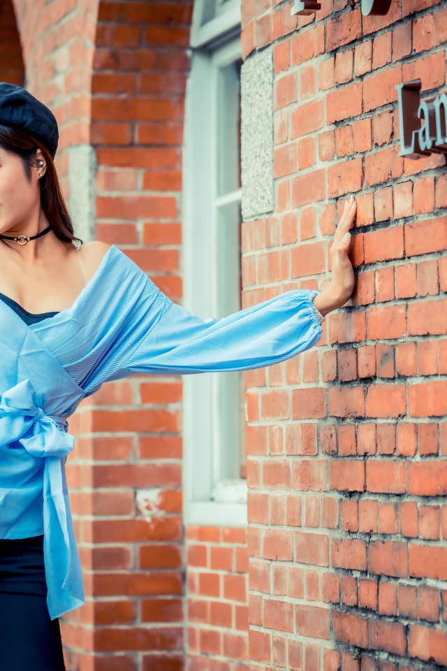 Молодая азиатка в черном берете стоит у стены 