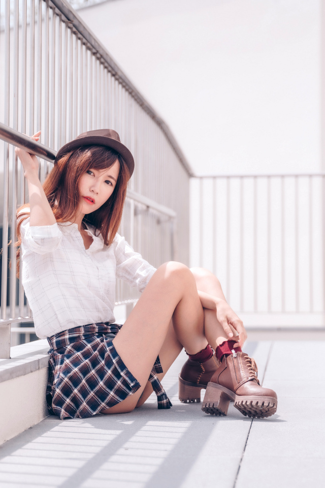 Молодая азиатка в короткой юбке сидит у перил 