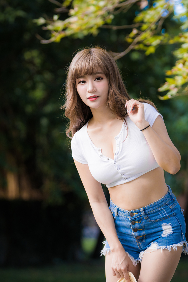 Молодая азиатка в белом топе и синих шортах  в парке