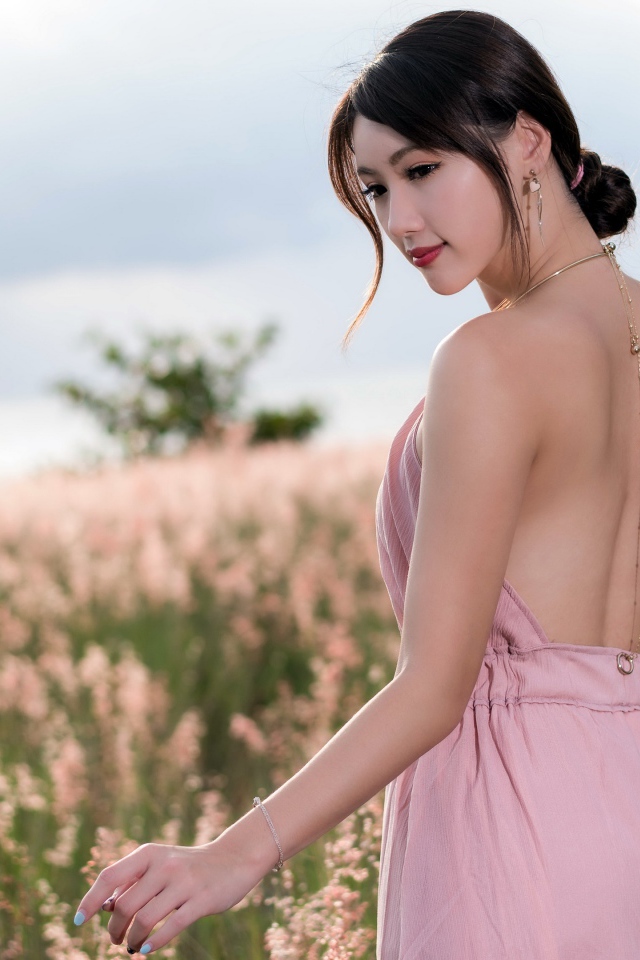 Молодая азиатка в розовом платье гуляет по полю с колосьями