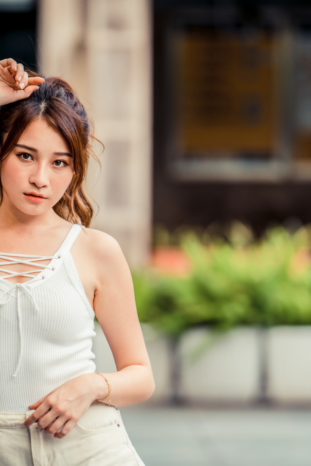 Молодая красивая азиатка в белой майке стоит у ворот