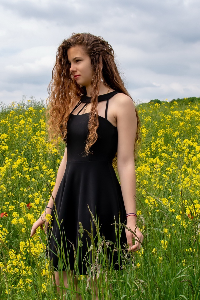 Молодая девушка в черном платье на поле с желтыми цветами