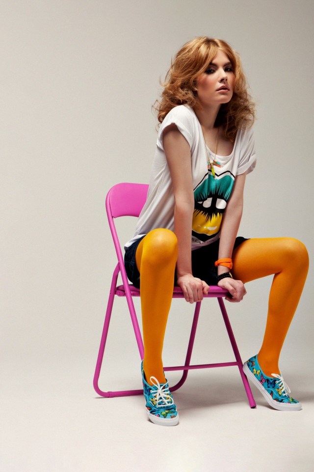 Молодая девушка в ярком костюме сидит на розовом стуле