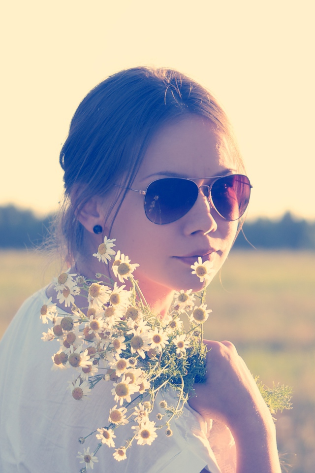 Молодая девушка в солнечных очках с букетом ромашек на поле