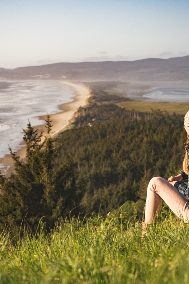 Молодая девушка сидит на зеленой траве на фоне моря