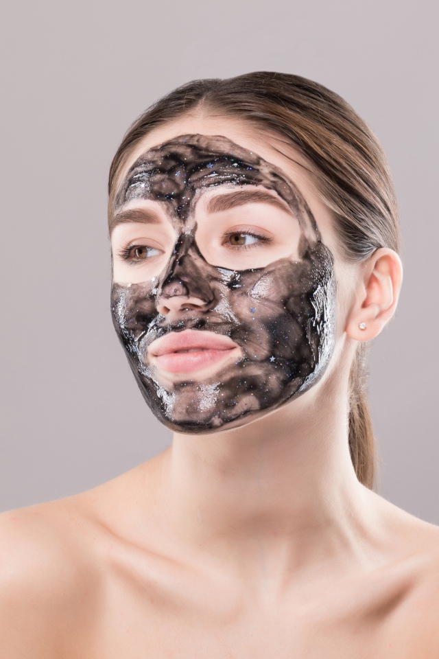 Молодая девушка с косметической черной маской на лице