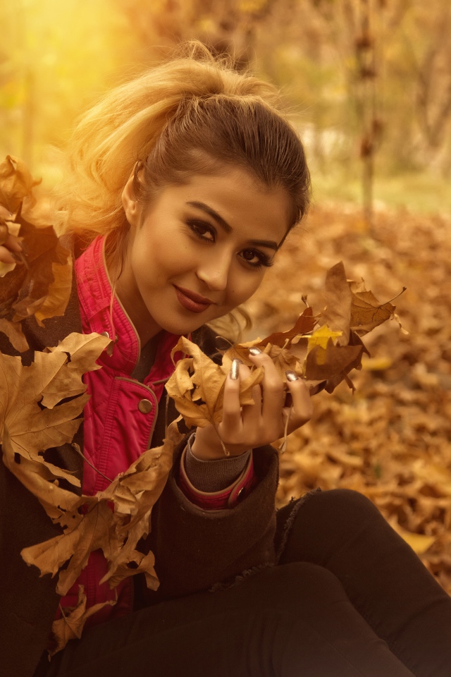 Молодая девушка с опавшими листьями в руках в парке