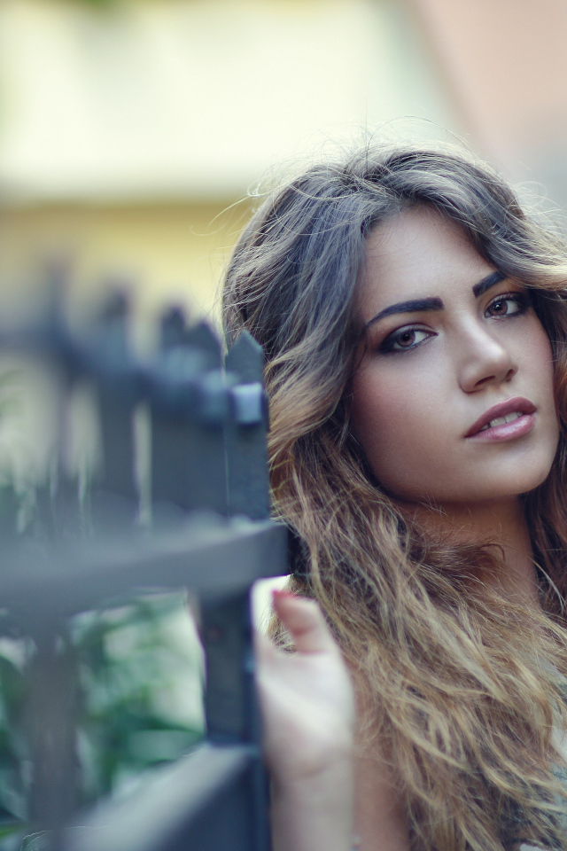 Молодая девушка с длинными волосами стоит у забора