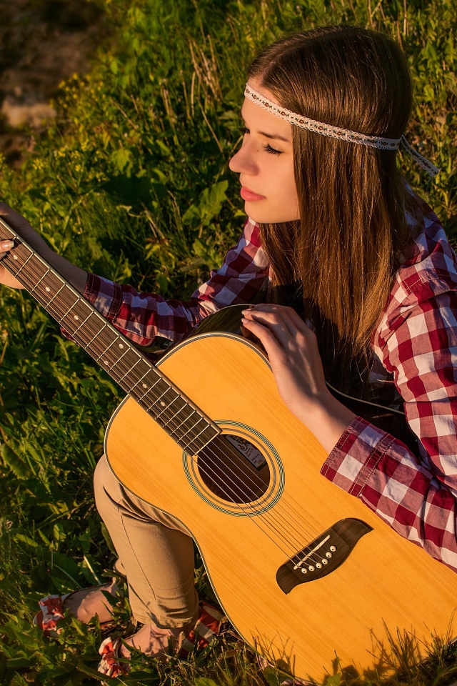 Молодая девушка хиппи сидит с гитарой на траве 