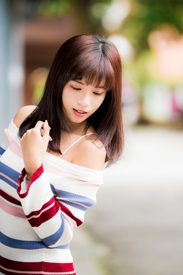 Молодая нежная девушка азиатка в свитере стоит у забора 