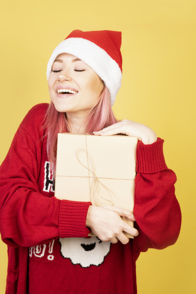 Улыбающаяся девушка в красном свитере с подарком на желтом фоне