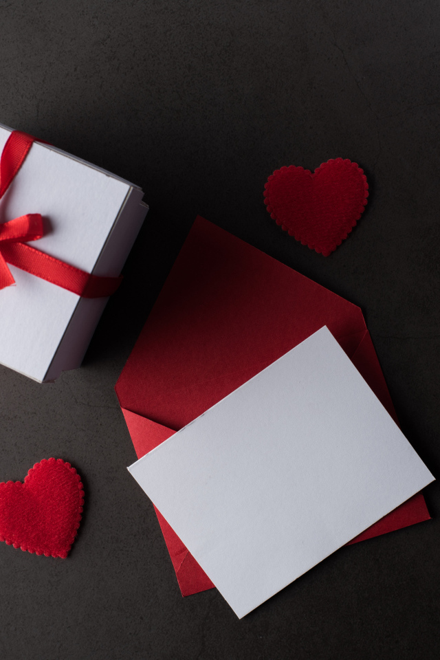 Envelope and gift on a gray table with red hearts.