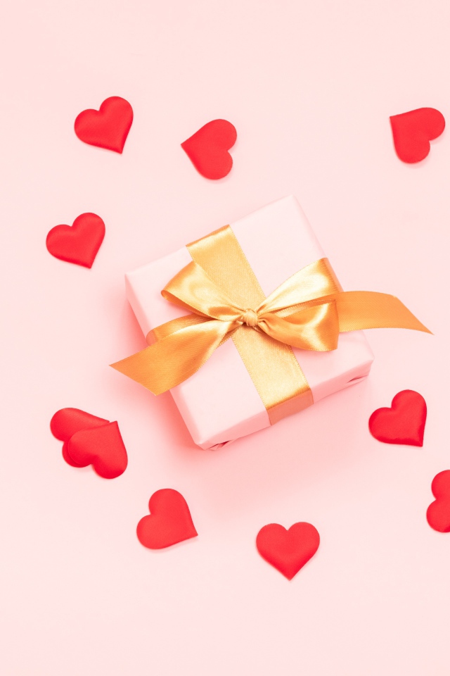Подарок с бантом на розовом фоне с красными сердечками