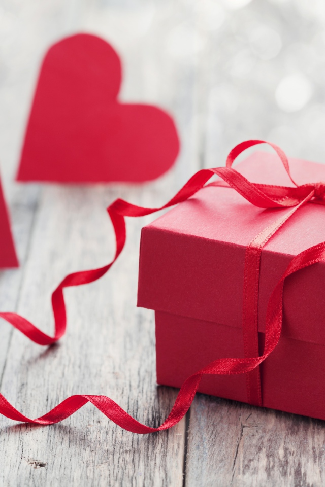 Красная коробка с подарком на столе с красными сердечками