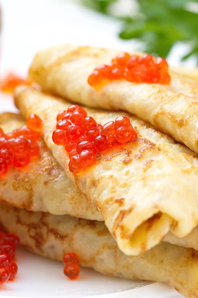 Аппетитные тонкие блины с красной икрой на тарелке с петрушкой угощение на Масленицу