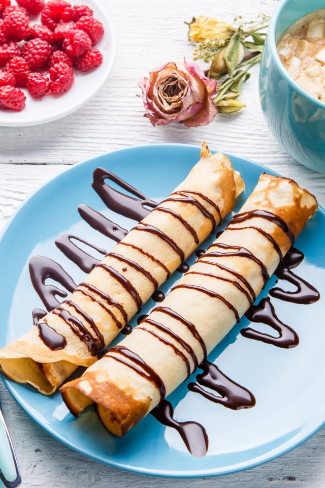 Тонкие блины с шоколадом на столе с ягодами малины и какао 