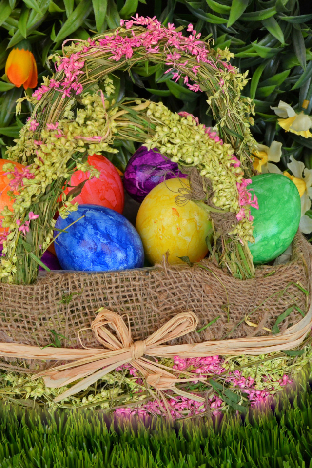Разноцветные пасхальные яйца в корзине на зеленой траве на праздник 