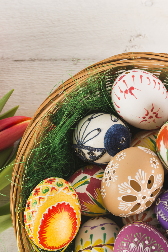 Разноцветные крашеные яйца в корзине с букетом тюльпанов на Пасху