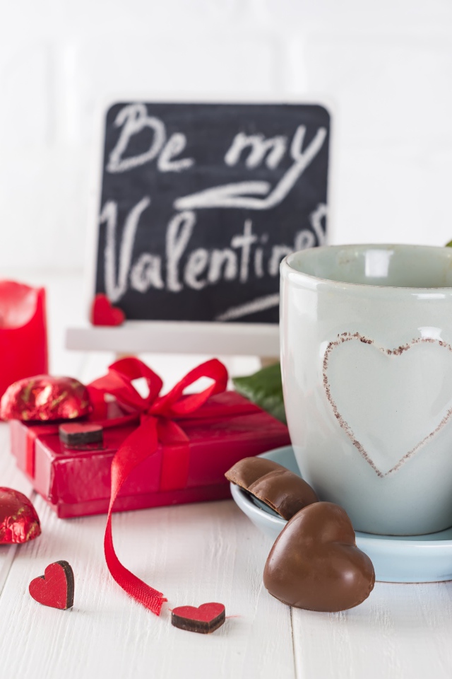 Белая чашка с конфетами и красной розой на столе в подарок на 14 февраля
