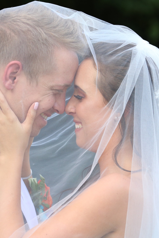 Жених и невеста стоят под белой фатой