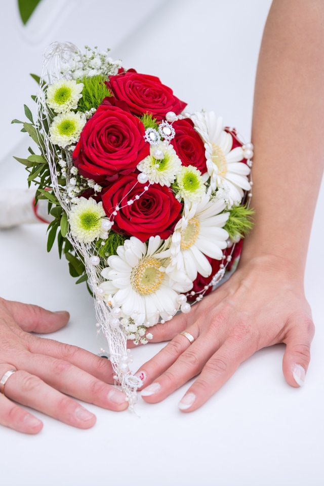 Две руки с обручальными кольцами и свадебным букетом