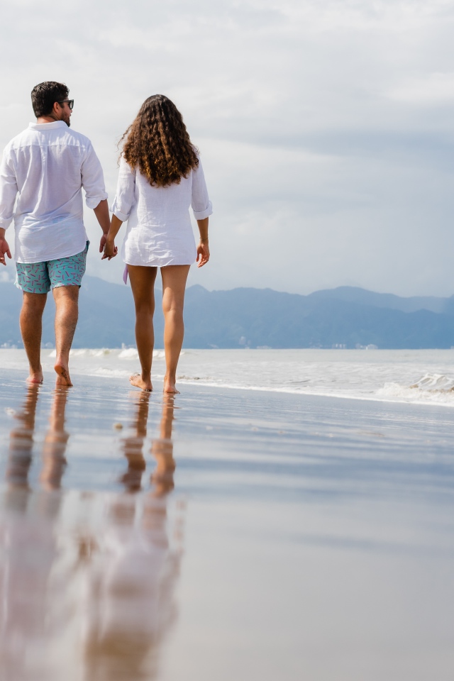 Влюбленная пара идет по мокрому песку у моря 