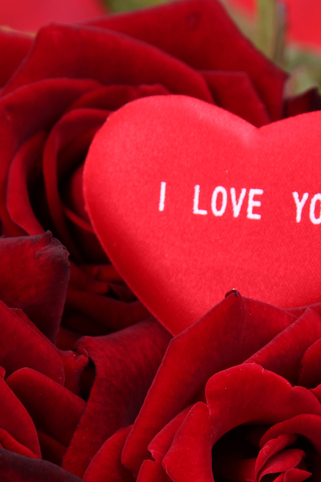 Маленькое сердце лежит на букете красных роз 