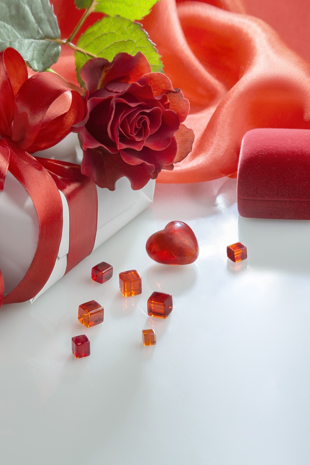 Подарки на белом столе с розой и красной тканью