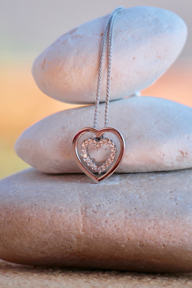 Золотой кулон в форме сердца висит на камнях 