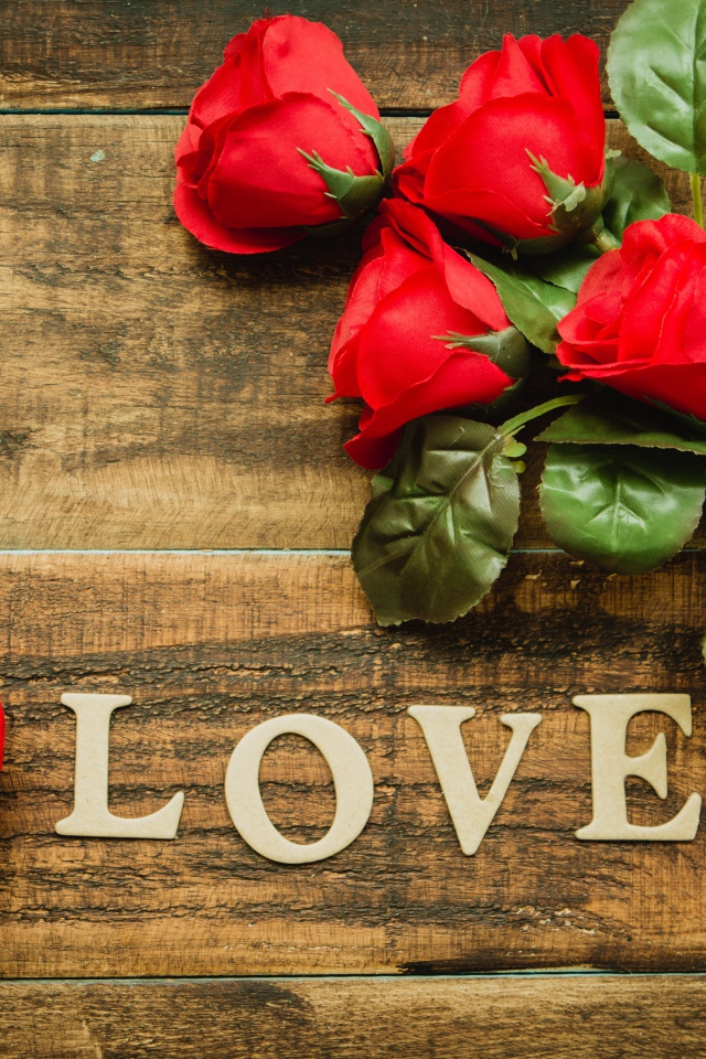 Надпись LOVE на столе с розами и красным сердцем
