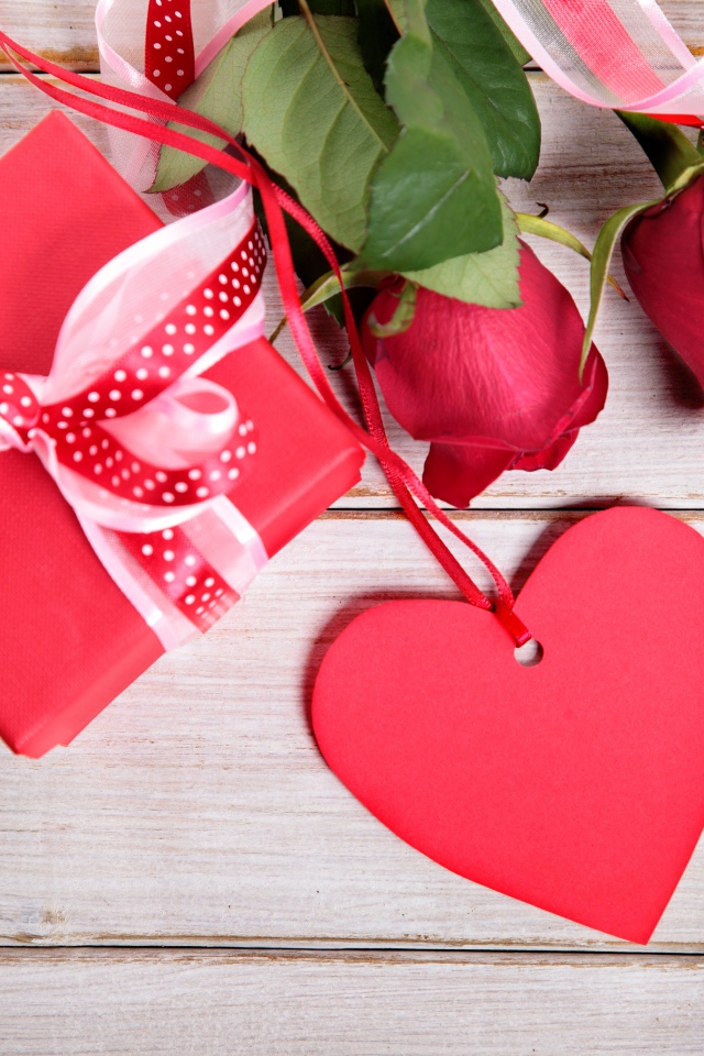 Красные розы с подарком и красным сердцем на деревянном столе
