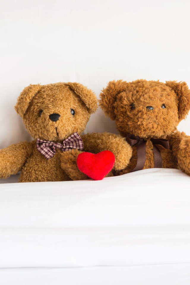 Два медвежонка Тедди лежат на кровати под одеялом 